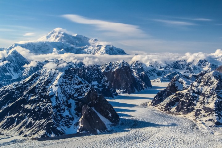 Aerial view of snow-covered mountains and glaciers under a clear blue sky.