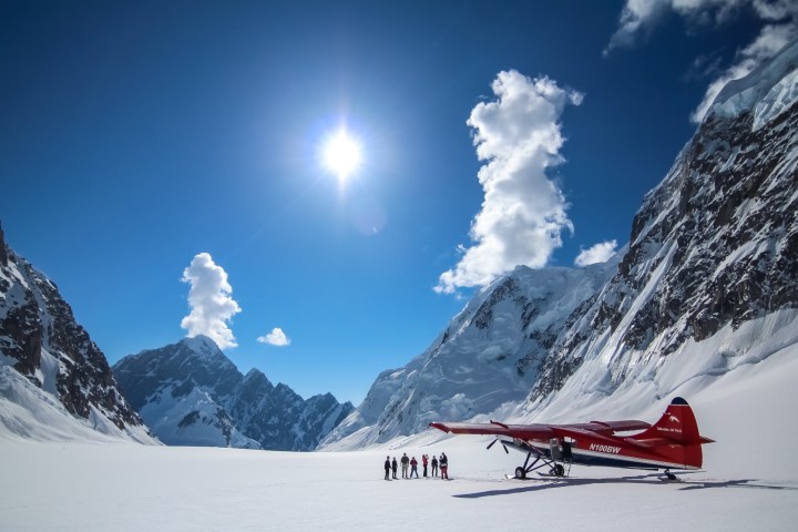 Red plane on snowy mountain landscape with people and clear blue sky.
