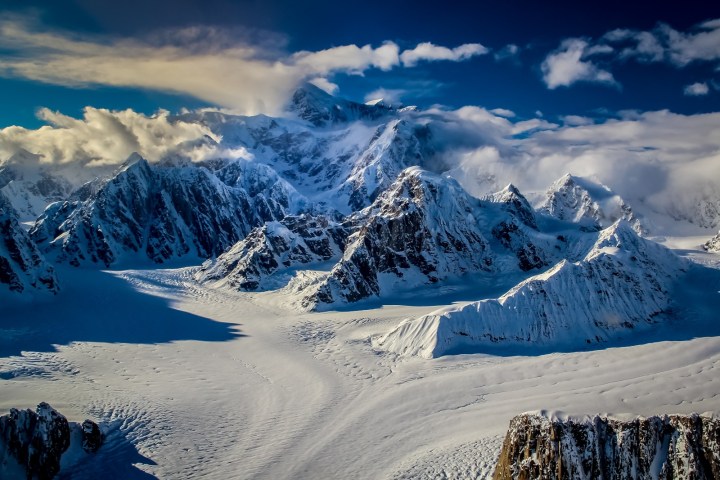 Snow-covered mountains with a glacier under a partly cloudy sky.