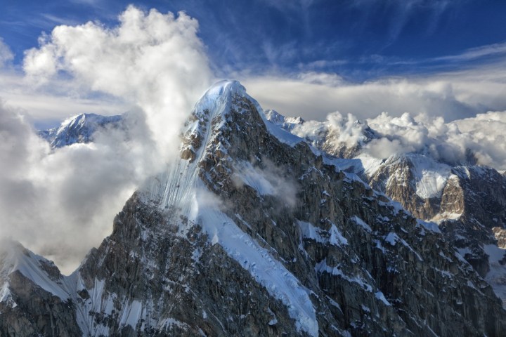 Snow-capped mountain peak surrounded by clouds and blue sky.