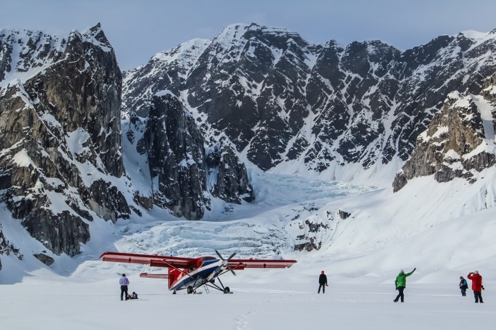 Small plane on snowy glacier surrounded by mountains.