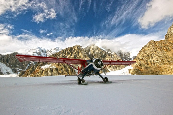 Small plane with red wings on snow, mountains in background.