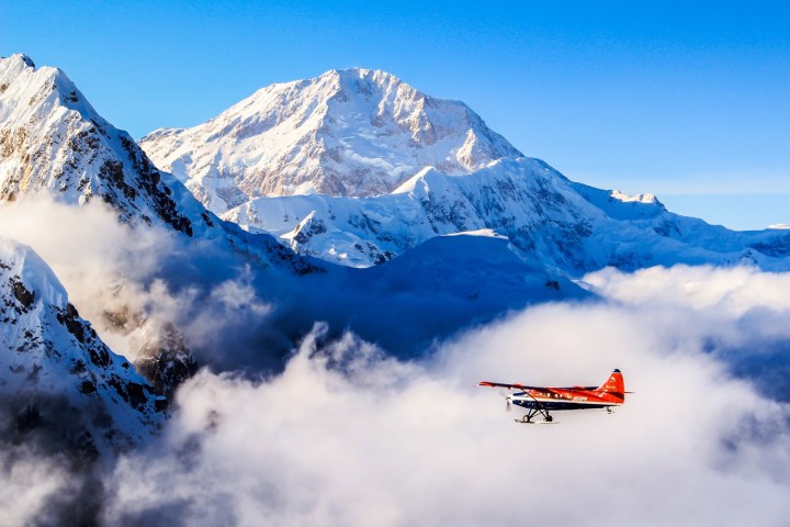 Red plane flying over snow-covered mountains and clouds.