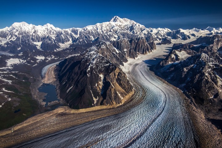 Snowy mountain range with a winding glacier and a lake.