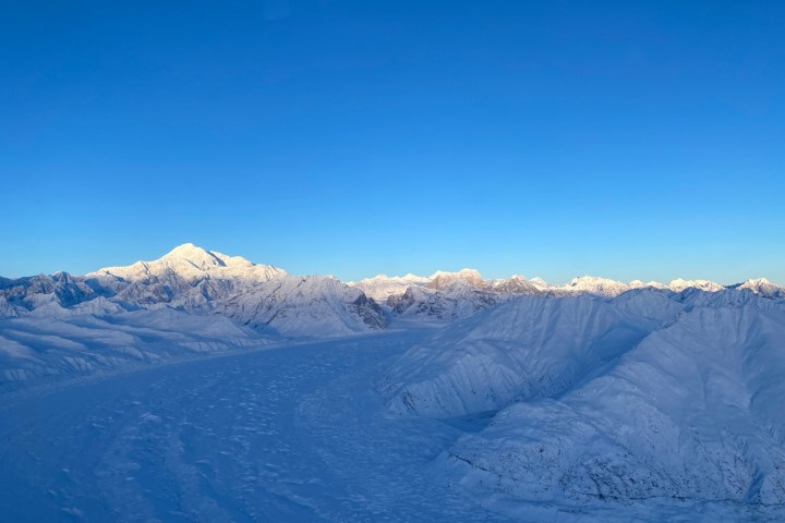 Snow-covered mountains under a clear blue sky at sunrise.