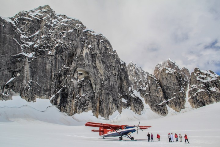 Small plane and group of people on snowy mountain landscape.