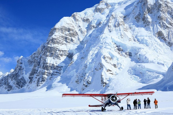 Small red plane on snowy mountain with people nearby.