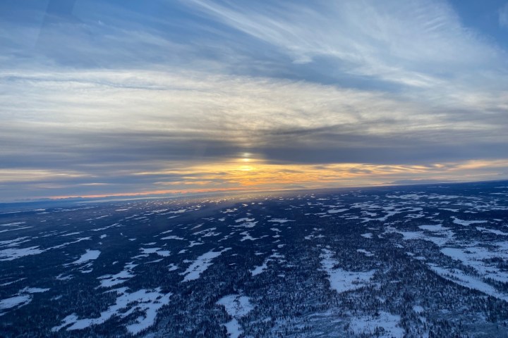 Aerial view of snowy landscape at sunset with cloudy sky.